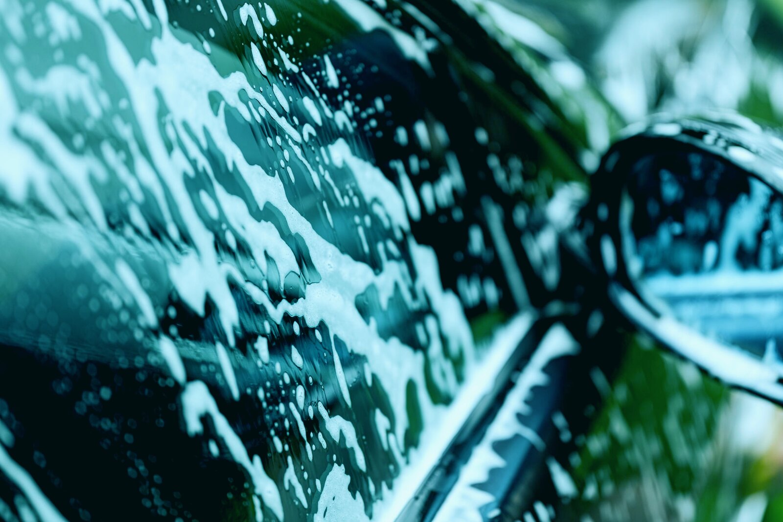 Close up of a dark car covered in white foam suds during an automated car wash cycle
