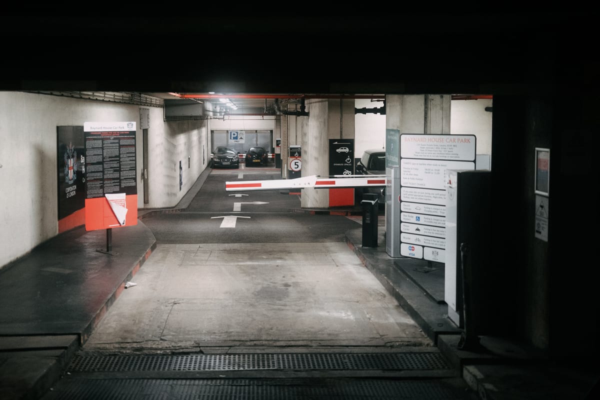 A car park entrance with signage and a security barrier, the signage layer the April 2026 revision re timetabled