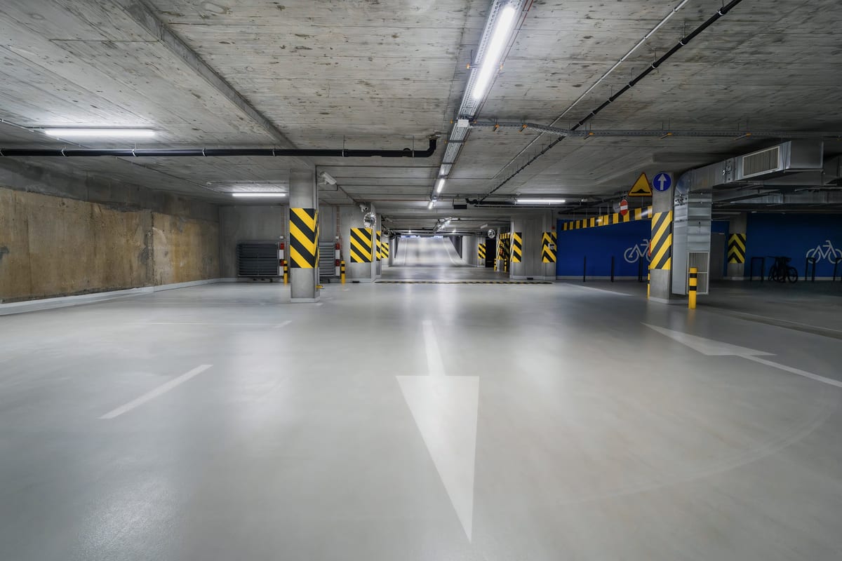 A white directional arrow painted on the floor of a well lit car park guiding drivers toward free spaces